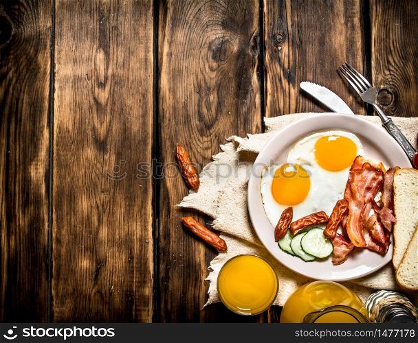 Breakfast in the morning. Fried bacon with eggs and orange juice. On a wooden table.. Fried bacon with eggs and orange juice.