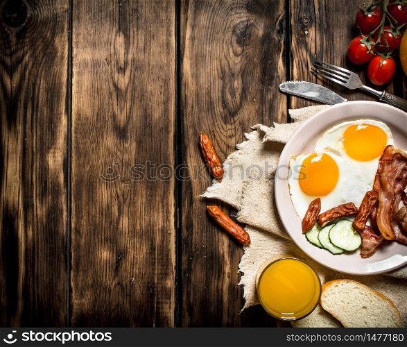 Breakfast in the morning. Fried bacon with eggs and orange juice. On a wooden table.. Fried bacon with eggs and orange juice.