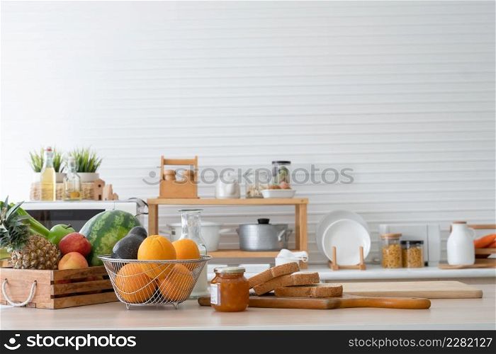 Breakfast ingredients are on kitchen table at home, including sliced whole wheat bread, jam, oranges, avocados, watermelon, red and green apples, pineapples and vegetables for fresh juices and salads