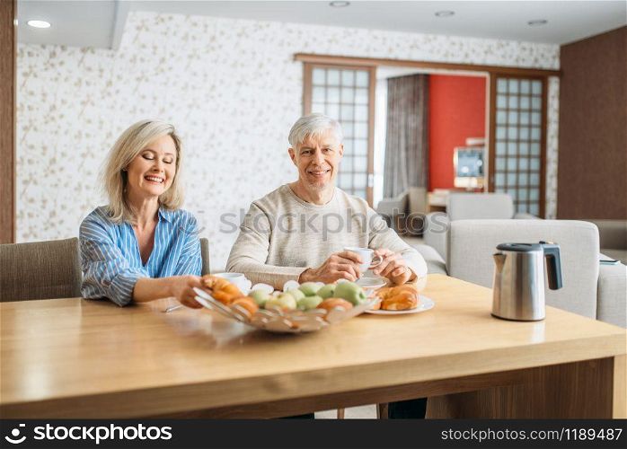 Breakfast of adult love couple at home. Mature husband and wife sitting in the kitchen, happy mature family, man and woman drinks coffee at the table with fruits. Breakfast of adult love couple at home