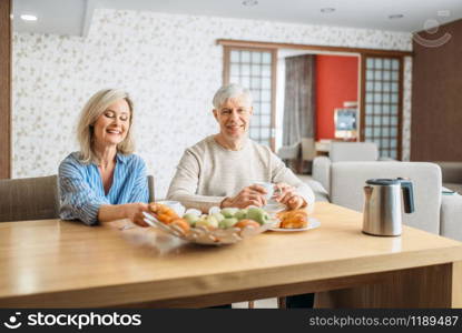 Breakfast of adult love couple at home. Mature husband and wife sitting in the kitchen, happy mature family, man and woman drinks coffee at the table with fruits. Breakfast of adult love couple at home