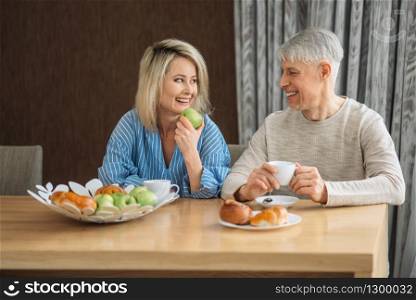 Breakfast of adult love couple at home. Mature husband and wife sitting in the kitchen, happy family, man and woman drinks coffee at the table with fruits