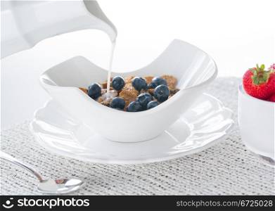 Breakfast of blueberries, bran flakes strawberries in modern pottery bowl with milk jug