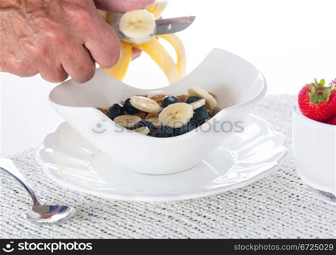 Breakfast of blueberries, bran flakes strawberries with banana being sliced