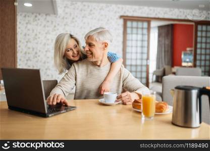 Breakfast of cheerful adult love couple at home. Mature husband and wife at the laptop in the kitchen, happy family