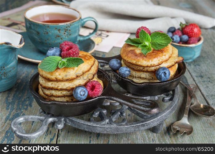 Breakfast of pancakes, fresh raspberries, blueberries and black tea in blue ceramic vintage cup, in rustic style