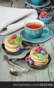 Breakfast of pancakes, fresh raspberries, blueberries and black tea in vintage cup, in rustic style