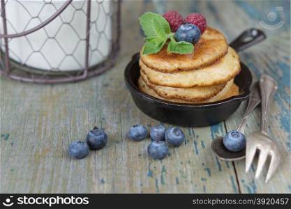 Breakfast of pancakes in cast-iron frying pan, fresh berries and milk in rustic style