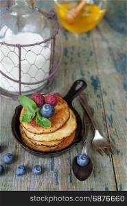 Breakfast of pancakes in cast-iron frying pan, fresh berries honey and milk in rustic style