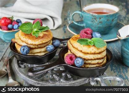 Breakfast of pancakes in cast-iron frying pans, fresh berries and black tea, in rustic style