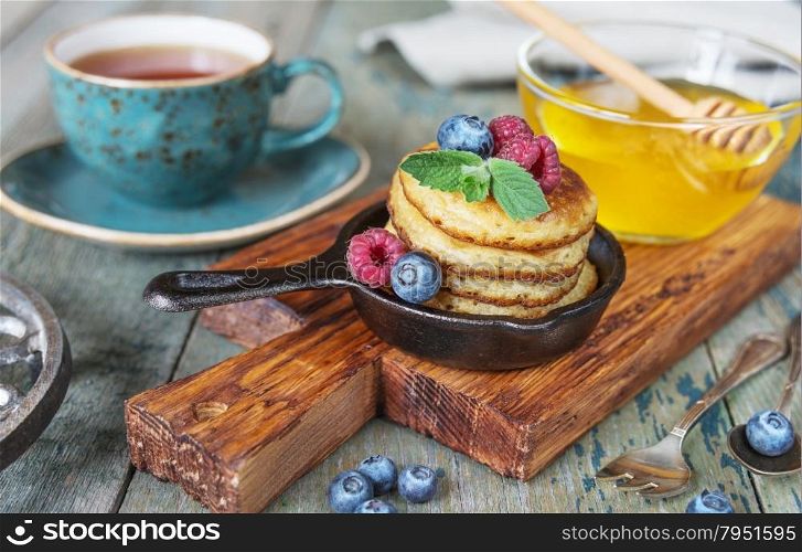Breakfast of pancakes in cast-iron frying pans, fresh berries and black tea in rustic style