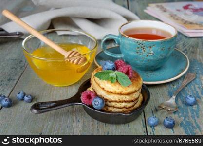 Breakfast of pancakes in cast-iron frying pans, fresh berries, honey and black tea in rustic style