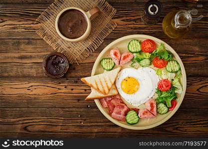 Breakfast on Valentine&rsquo;s Day - fried egg in the shape of a heart, toasts, sausage, bacon and fresh vegetables. English breakfast. Cup of coffee. Top view