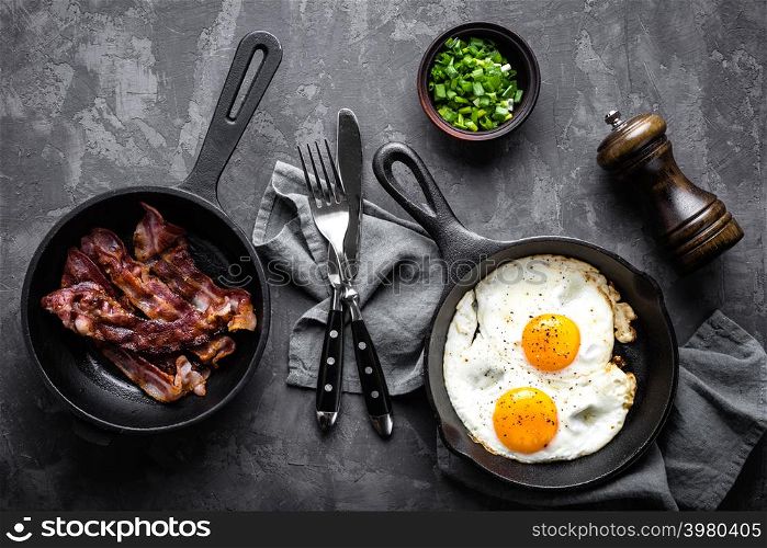 breakfast or brunch fried bacon and eggs in black skillets and top view. breakfast or brunch fried bacon and eggs in black skillets top view