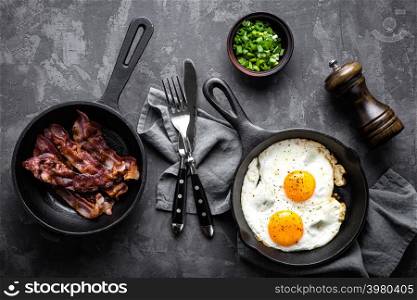 breakfast or brunch fried bacon and eggs in black skillets and top view. breakfast or brunch fried bacon and eggs in black skillets top view