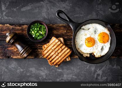 breakfast or brunch fried eggs in black skillet and crispy toasts top view with space for a text