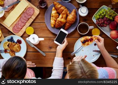 breakfast, people and technology concept - women with smartphones eating and photographing food at table. women with smartphones eating food at table