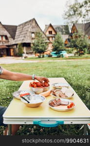 Breakfast prepared during summer vacation on c&ing. Bread, cottage cheese, cold meat, tomatoes, fruits and coffee cups on table. Close up of outdoor table setting set on grass. Breakfast prepared during summer vacation on c&ing