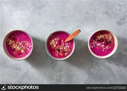 Breakfast red smoothie bowl topped with berry, beets and oatmeal with almonds on a concrete background, flat lay. Red smoothie bowls with beets, granola, flax seeds and berries for tasty and healthy breakfast on stone background