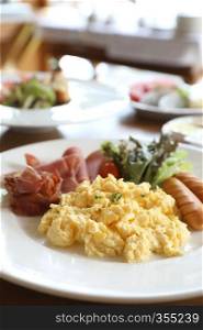 Breakfast scrambled egg with bacon sausage and salad on wood background