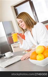 Breakfast - Smiling woman reading newspaper in kitchen, with coffee and fresh orange juice