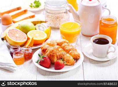 Breakfast table with croissants, coffee, orange juice, toasts and fruits