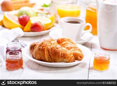 Breakfast table with croissants, coffee, orange juice, toasts and fruits