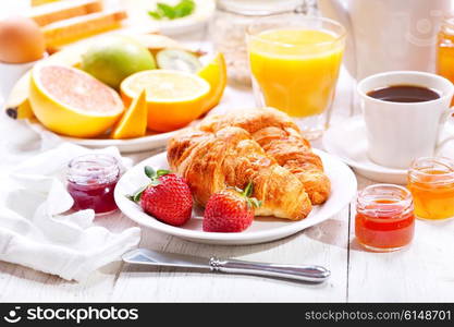 Breakfast table with croissants, coffee, orange juice, toasts and fruits