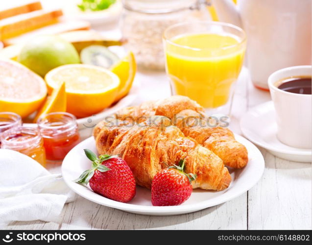 Breakfast table with croissants, coffee, orange juice, toasts and fruits