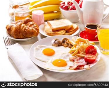 Breakfast table with fried eggs, coffee, orange juice, toasts and fruits