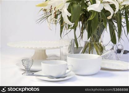 Breakfast tablesetting with bright white crockery and lily flwoers. White breakfast table setting with lily flowers