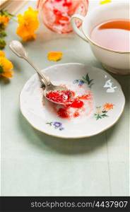 Breakfast tea with plate of red jam, spoon and garden flowers, close up