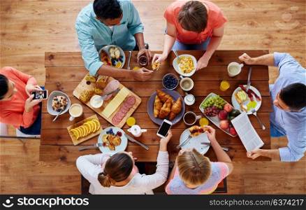 breakfast, technology and family concept - group of people with smartphones eating and photographing food at table. people with smartphones eating food at table