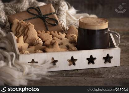 Breakfast tray with a cup of coffee, gingerbread cookies, and hazelnuts candies, a Christmas gift and a woolen scarf, on a rustic wooden table.