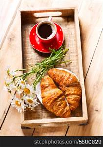 breakfast tray with croissants, cup of coffee and daisy flowers on wooden table