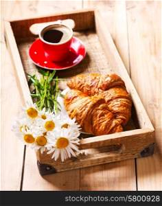 breakfast tray with croissants, cup of coffee and daisy flowers on wooden table