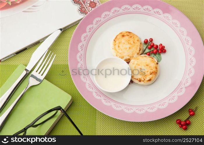 breakfast with berries on the plate with book and glasses and cutlery on a green tablecloth. Breakfast and a book on a green tablecloth
