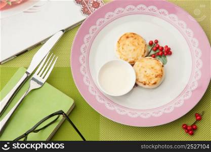 breakfast with berries on the plate with book and glasses and cutlery on a green tablecloth. Breakfast and a book on a green tablecloth