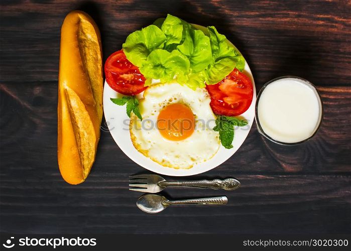 Breakfast with bread, fried eggs, milk and vegetables and fried tomato pieces on wood background