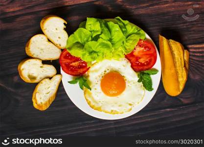 Breakfast with bread, fried eggs, milk and vegetables and fried tomato pieces on wood background