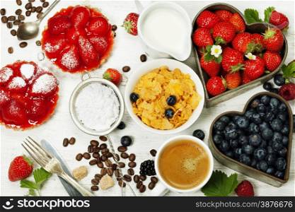 Breakfast with coffee, corn flakes, milk, tartlets and berry on wooden background