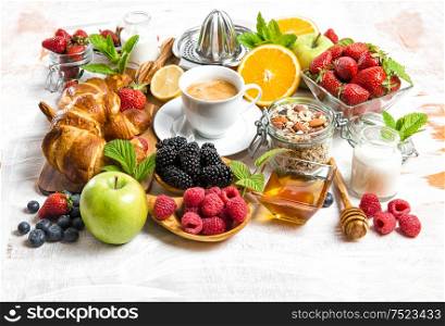 Breakfast with coffee, croissants, muesli, milk, fresh berries, fruits orange, apple. Healthy food concept