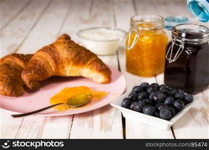 Breakfast with croissant, blueberries, yogurt and jam over a wooden table. Breakfast with croissant over a wooden table