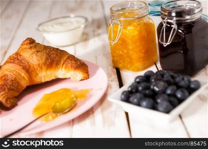 Breakfast with croissant, blueberries, yogurt, orange and blueberry jam over a wooden table. Breakfast with croissant over a wooden table