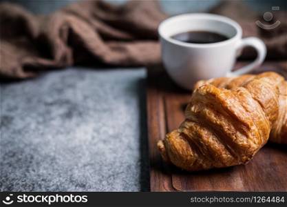 Breakfast with fresh croissants and cup of black coffee on wooden board