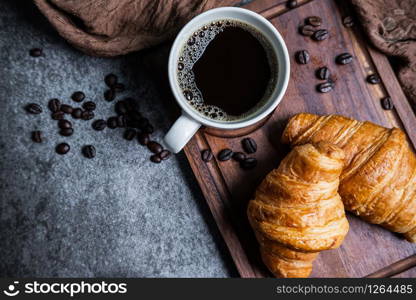 Breakfast with fresh croissants and cup of black coffee on wooden board