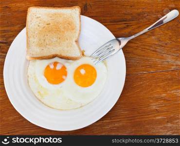 breakfast with fresh toast and two fried eggs on white plate on wooden table