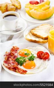 Breakfast with fried eggs, coffee, orange juice, croissant, toasts and fruits