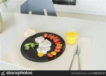 Breakfast with poached eggs and tomatoes on white kitchen table. Breakfast with poached eggs