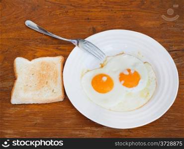 breakfast with two fried eggs on white plate and toast on wooden table